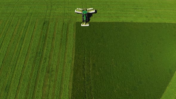 Aerial View Over Green Tractod Mowing Vivid Saturated Green Field of Wheat