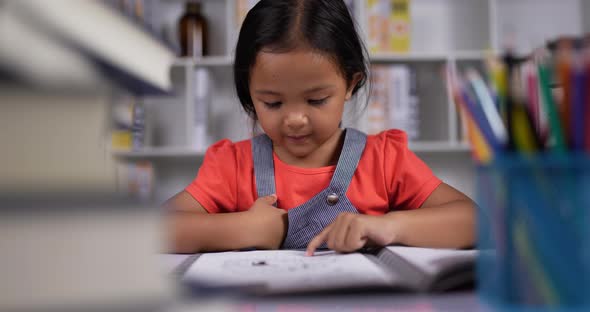 Asian little girl practicing reading at the desk at classroom.