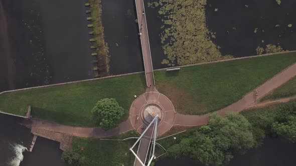 Aerial fly over of a bridge over a river dam by a grassy field