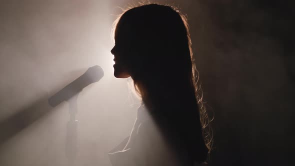 Close-up of the Face of the Singer with Microphone on a Black Smoky Background. The Singer Sings a