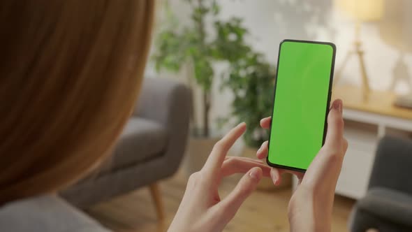 Point of View of Young Woman at Home Living Room Using With Green Mockup Screen Smartphone