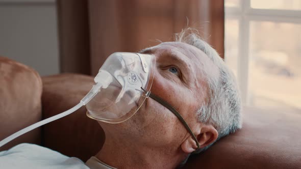 Sick Senior Man Breathing Through Inhalator Mask Lying At Home
