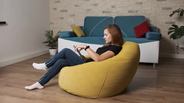 Woman Is Sitting on a Yellow Bean Bag and Talking with Friends Using a Tablet.