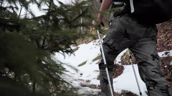 Backpacker in hiking gear with trekking poles walking up outdoor trail with snow. Slow motion