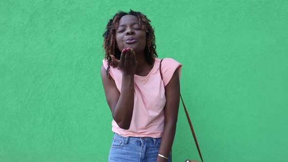 happy African-American woman dances and blows a kiss, on a green background