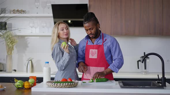 Front View Portrait of Cheerful Caucasian Woman Taking Apple As African American Man in Apron