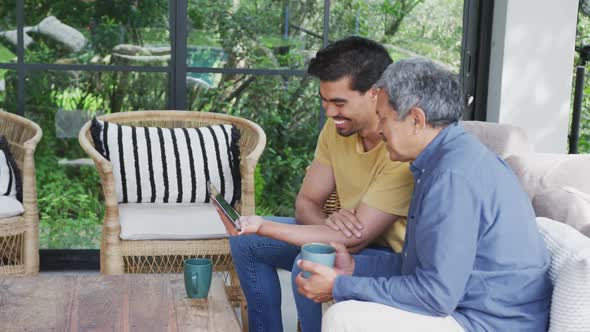 Biracial father and son having coffee while watching video on digital tablet at patio