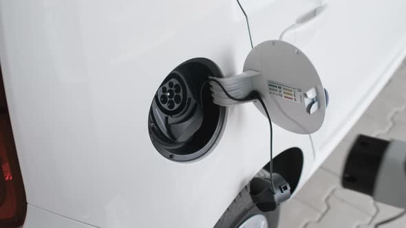 Woman Inserts a Power Cord Into an Electric Car for Charging