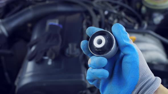 master in glove holds lever silent block in his hand against background engine.