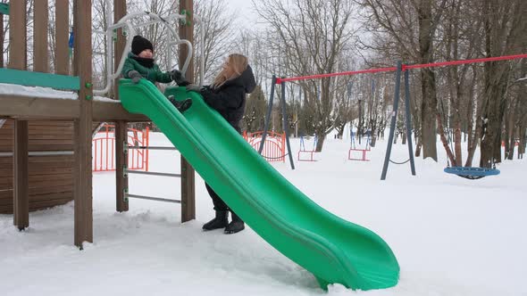 Young Mother Helps Her Son Slide Down the Hill