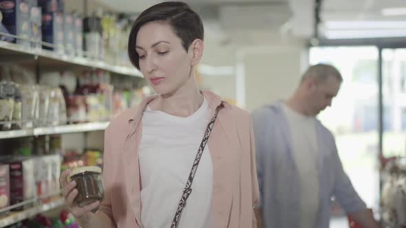 Portrait of Beautiful Concentrated Woman Putting Canned Food Into Basket in Grocery, Caucasian