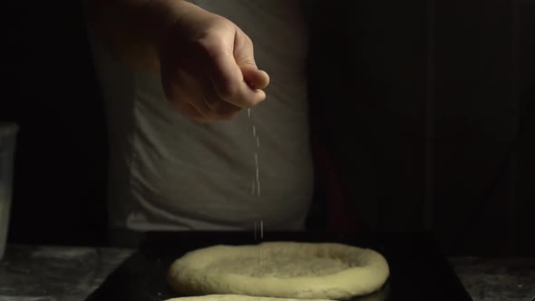 Tattooed hand pours sesame seeds or salt on bread,