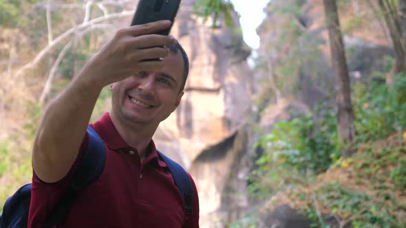 Smiling Male Traveler Takes Selfies on Phone Against Canyon in a National Park