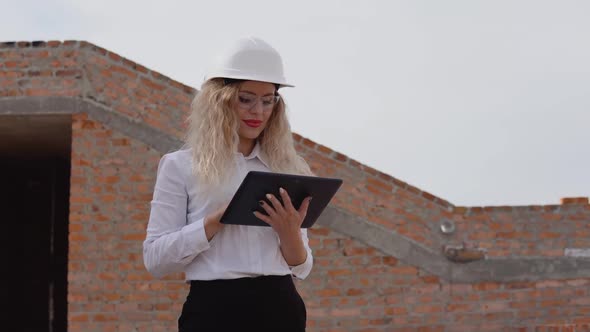 Female Architect in Business Attire Stands in a Newly Built House with Untreated Walls and Works on