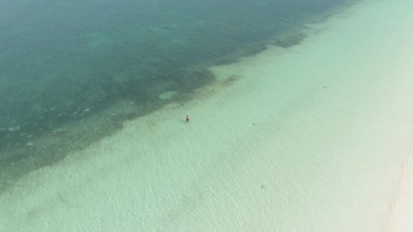 Aerial: woman walking in turquoise water white sand tropical beach coral reef Pa
