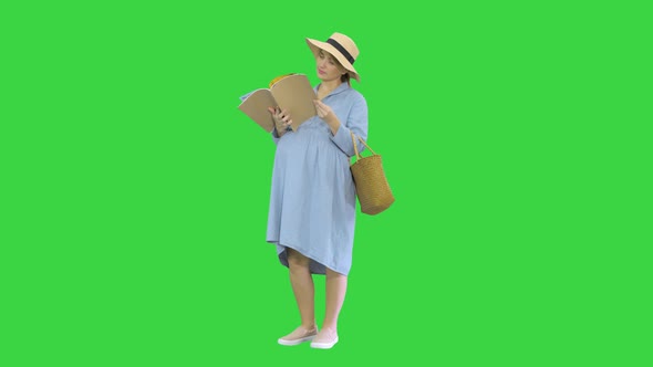 Pregnant Woman in a Summer Hat Reading Magazine on a Green Screen, Chroma Key.