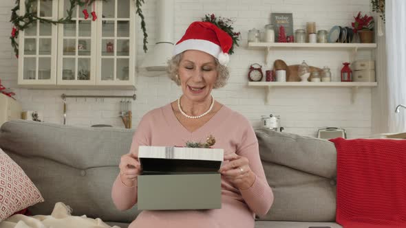 Elderly Woman in Hat Holds Box on Knees and Opens Present