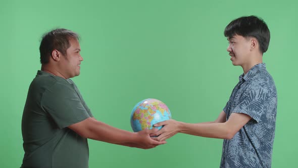 Asian Man Hand In The World Globe To Adult Man While Standing In Front Of Green Screen Background