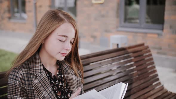 a girl reads a book on a street bench