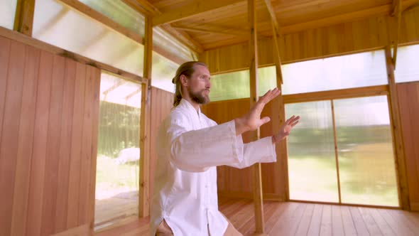 A Caucasian Bearded Man with Long Blond Hair Practices Qigong and Taichi in a Wooden Practice Room