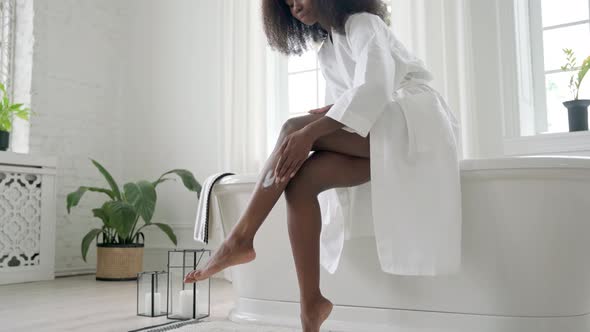 Black Woman Applies Moisturizing Cream Lotion on Legs in Bathroom