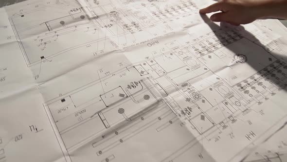 Blueprints of Oil and Gas Equipment Drawings. Fingers of a Human Being Show Circuit on Printed