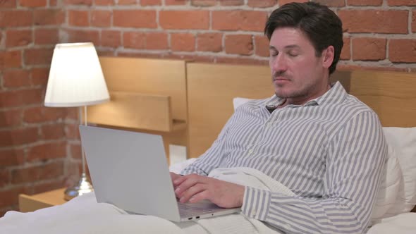 Middle Aged Man with Laptop Looking at the Camera in Bed