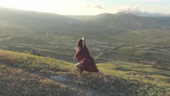 An Attractive Woman in a Red Dress Performs a Ritual Dance on the Top of a Hill in the Rays of the