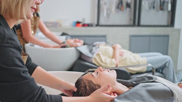 Asian young woman lying on salon washing bed getting hair washed in hair salon by beauty stylist.