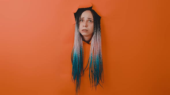 Young Woman with Multicolored Hairstyle Sticking Out of Hole of Orange Background