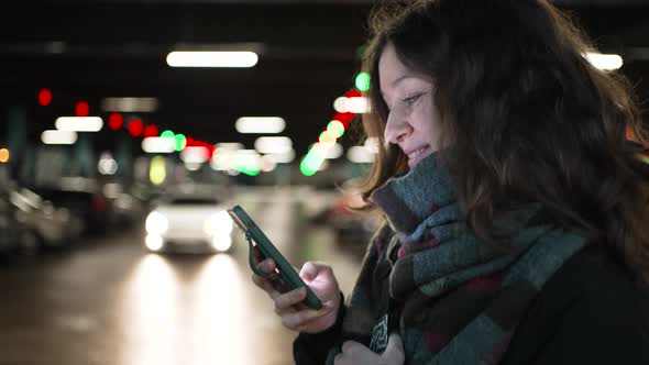 Portrait of a Young Woman with a Mobile Phone in Her Hands Walks Along the Parking of a Shopping