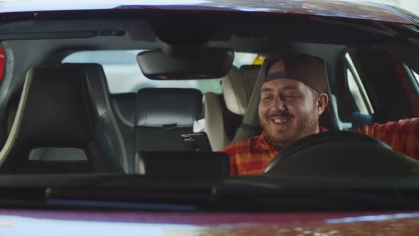 Stout Young Man Using Mobile Phone Sitting Behind Wheel of Car