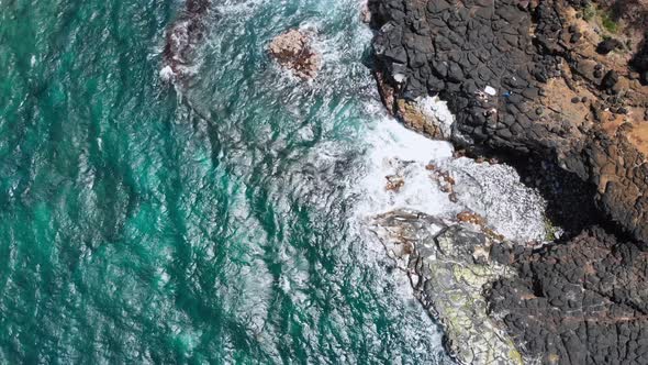 Drone camera approaching the waves of the ocean foaming off the rocky shore at Kauai, Hawaii, USA