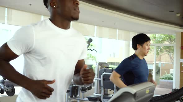 Multiethnic Asian and African American Males Running on Treadmills at Gym Club During Daytime