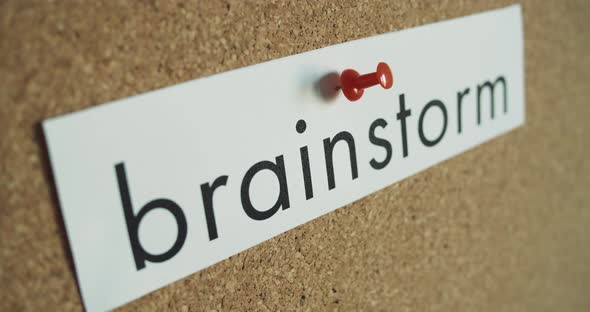 Sticky note: BRAINSTORM - Pinned to cork wall - and red