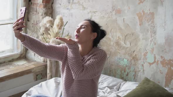 young beautiful girl chatting and posing on the smartphone and laughing while lying in bed at home