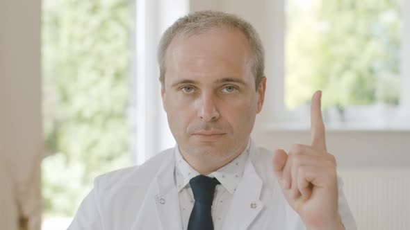 Close-up Portrait of Confident Serious Doctor Sitting with Raised Finger and Looking at Camera