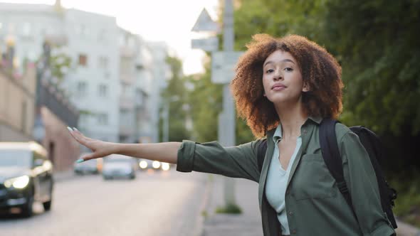 Beautiful African American Millennial Woman in Casual Wear Waving Down Car Hitchhiking on Roadside