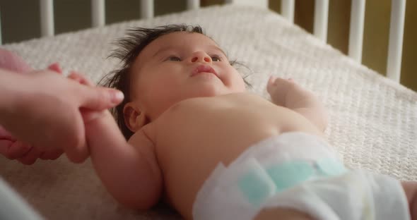 Caring Mother Stroking a Newborn Baby in a Diaper Lying on Her Back in Crib