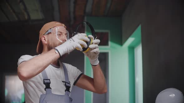 Male Builder Takes Off Safety Glasses and Headphones After Work in Studio