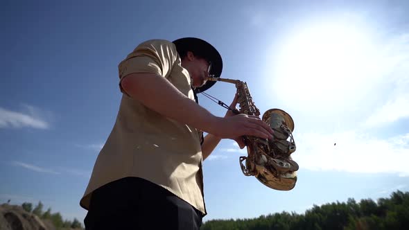 Saxophonist Is Playing Music at Nature, Tilt Up View Against Sky with Bright Sun