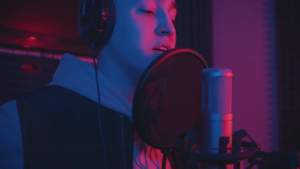 A Man in Hoodie Rapping Through the Pop-filter in the Microphone - Sound Recording Studio