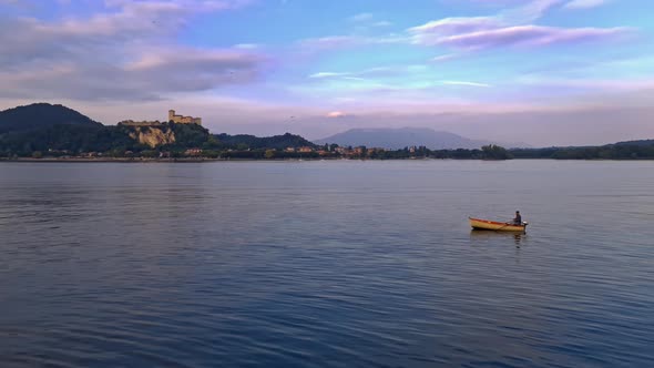 Small fishing rowing boat with fisherman onboard in calm lake waters of Maggiore lake in Italy with