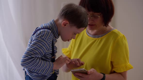 Side View Curios Autistic Boy Touching Smartphone with Blurred Woman Talking