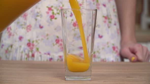 A Woman in the Kitchen Pours Fresh Juice From a Jug Into a Glass