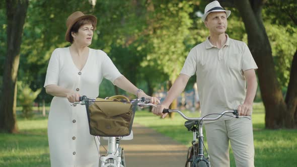 Positive Loving Mid-adult Man and Woman Walking with Bikes and Talking. Portrait