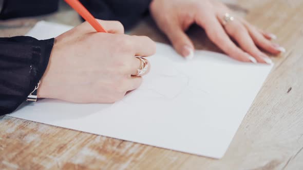 Female's hands drawing sketches of clothes on paper in her workplace.