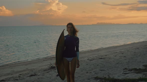 Young Attractive Female Surfer with Her Surfboard at Sunset on the Beach