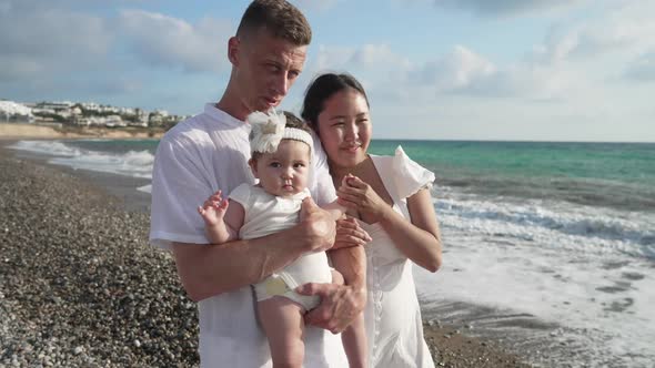 Happy Cute Baby Girl with Caucasian Father and Asian Mother on Picturesque Mediterranean Sea Coast