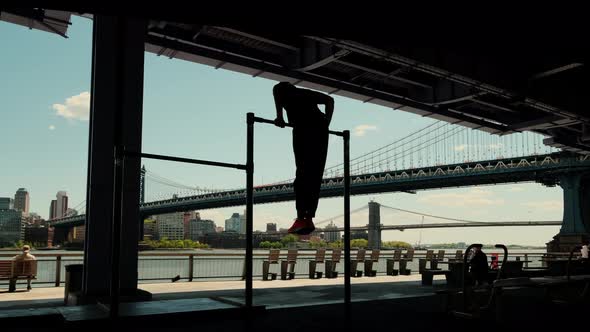 Silhouette of Disabled Young Man Pulled Up on the Crossbars in the Form of a City